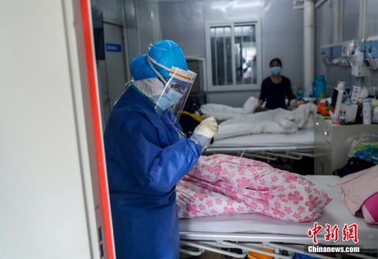 火神山医院感染二科一病区的隔离病房内医护人员为患者进行身体检查。中新社记者 张畅 摄